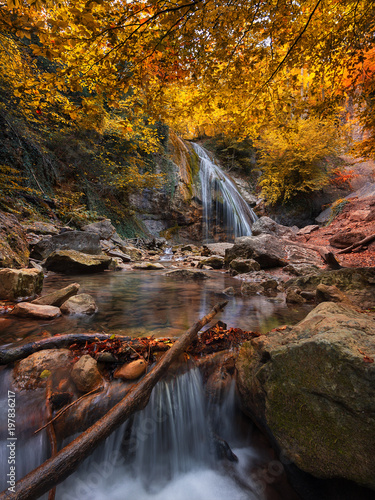 Vertical Amazing Landscape With Waterfall Among The Colorful Autumn Forest. Autumn Forest Landscape With Beautiful Cold Creek. Enchanted Autumn Forest With Falling Leaves On  Ground And Cold Stream