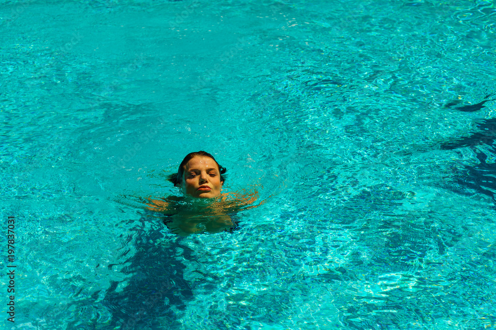 Beautiful tanned woman in swimwear relaxing in swimming pool