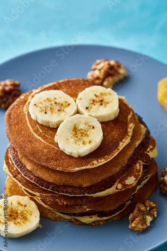 Pile of homemade pancakes with banana and walnuts on blue background, selective focus