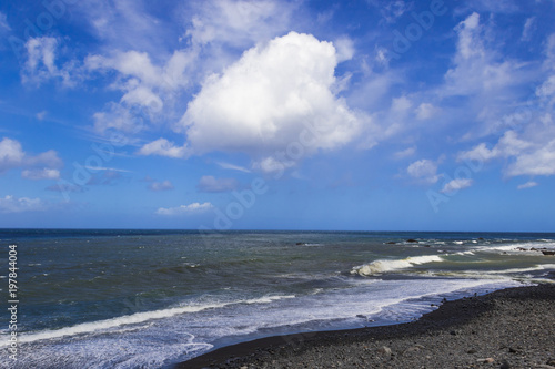 Waves of the Atlantic Ocean crushing the beach under the blue cloudy sky on a sunny day