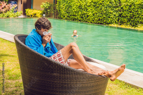 Sick man traveler. The man caught a cold on vacation, sits sad at the pool drinking tea and blows his nose into a napkin photo