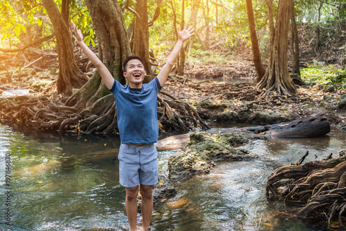 Relaxing for life natural therapy concept  Young man stands on rocks Stream river fast with raised arms up  smiling at forest for peachful. It show moisture tranquility  refreshing Travel of Thailand