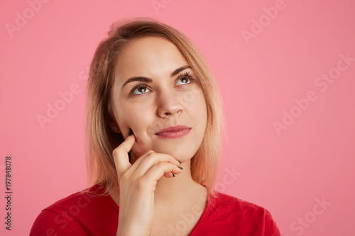 Close up shot of thoughtful dreamy young beautiful female looks pensively upwards, thinks about something pleasant, isolated over pink background. People, facial expressions and beauty concept