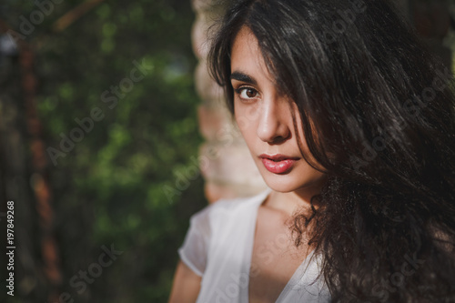 Lovely brooding brunette girl with long hair in a blooming spring garden under the warm rays of the sun. Close up.