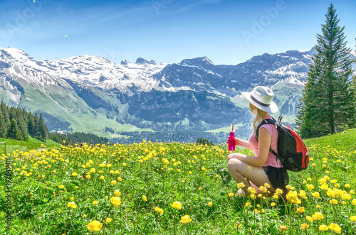 Swiss Alps. A girl sitting on the grass, drinking water from a bottle and admiring the mountain scenery. Engelberg Resort