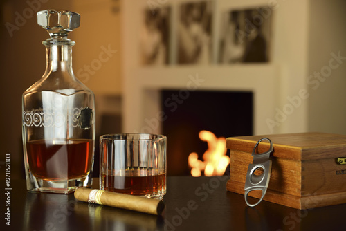 liqueur and cigar in the foreground on table and lit fireplace in the background