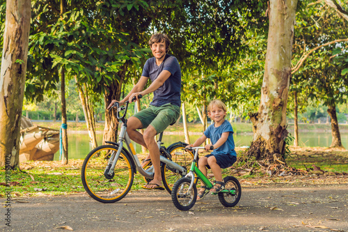 Happy family is riding bikes outdoors and smiling. Father on a bike and son on a balancebike photo