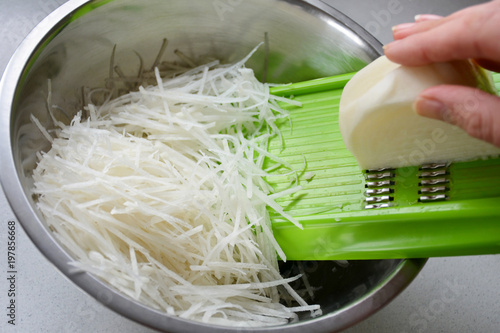 Photography Hand grating white vegetable root into stainless steel bowl