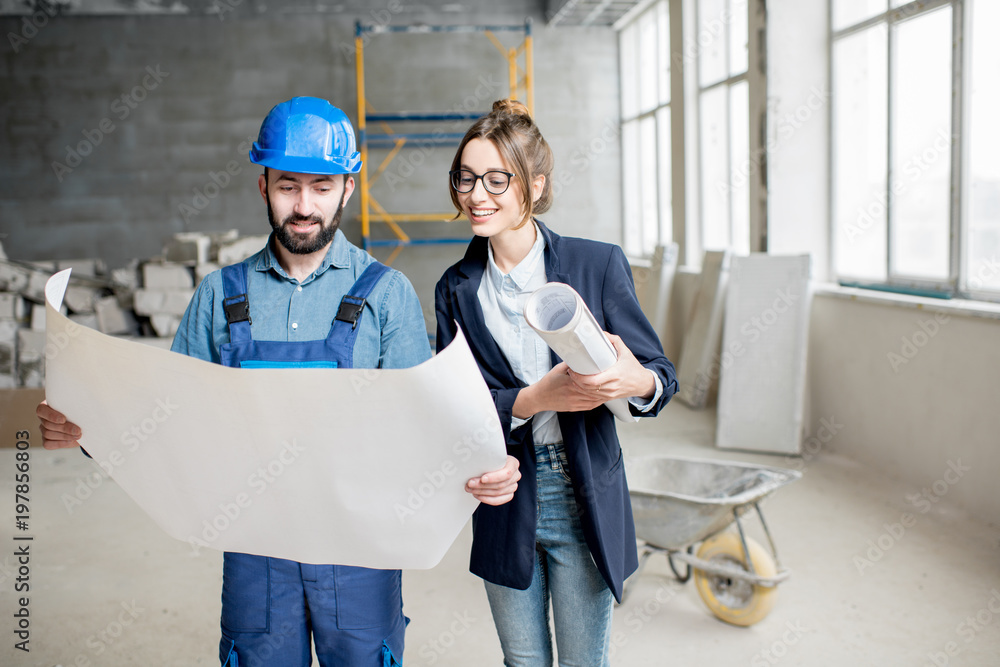 Foreman expertising the structure with businesswoman holding a blueprints at the construction site indoors Foreman expertising the structure with businesswoman holding a blueprints at the construction site indoors