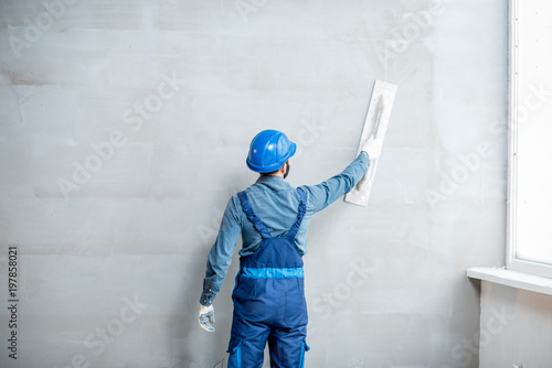 Plasterer in blue working uniform plastering the wall indoors photo