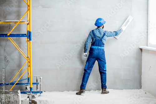 Plasterer in blue working uniform plastering the wall indoors photo