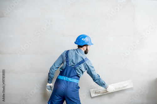 Plasterer in blue working uniform plastering the wall indoors photo