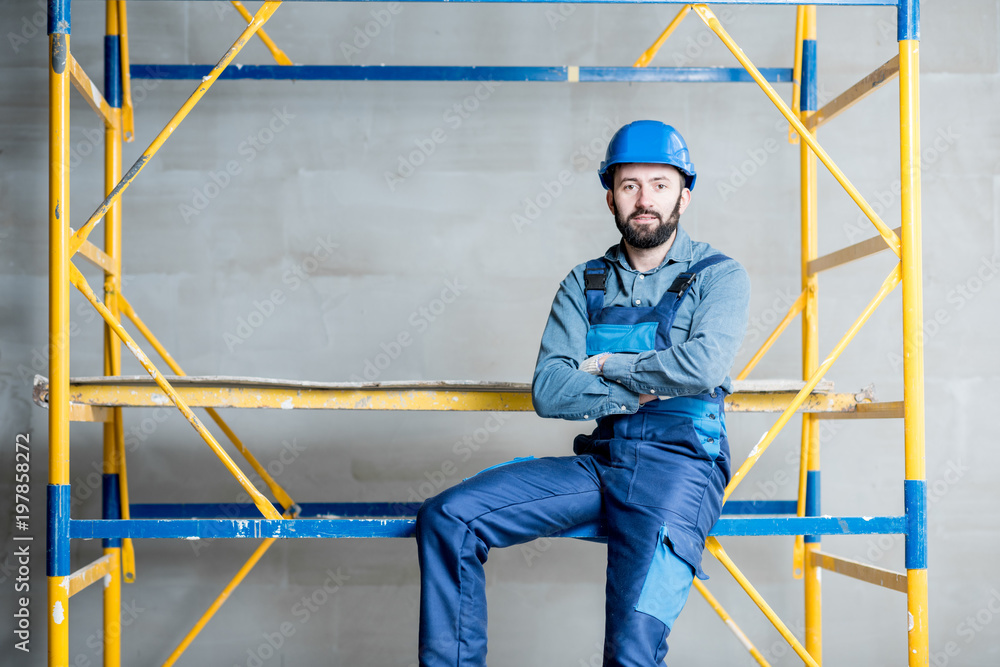 Builder in blue working uniform sitting on the scaffolding indoors Builder in blue working uniform sitting on the scaffolding indoors