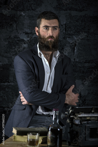 On chair sitting serious businessman. Dark hair and beard wearing jacket. Against the wall. © alexmina