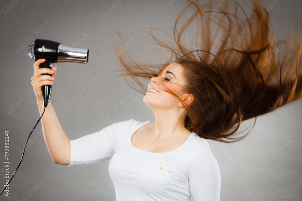 Woman drying her hair using hair dryer StockFoto Adobe Stock