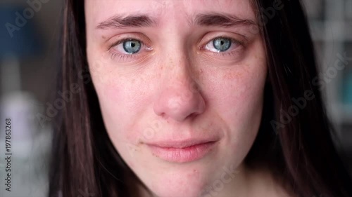 Young woman crying looking at the camera in slow motion. Tears comes out of an eyes
