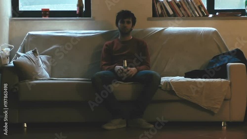 Shabby and lonely boy on a large sofa in a dark room.
