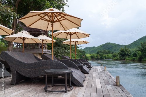 wooden deck with weaving sofa and white umbrella next to a river in Thailand