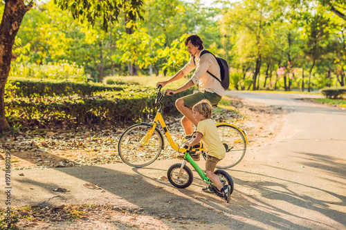 Happy family is riding bikes outdoors and smiling. Father on a bike and son on a balancebike photo