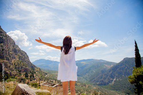 Young girl in white clothes standing on rock in Greece with view at mountains