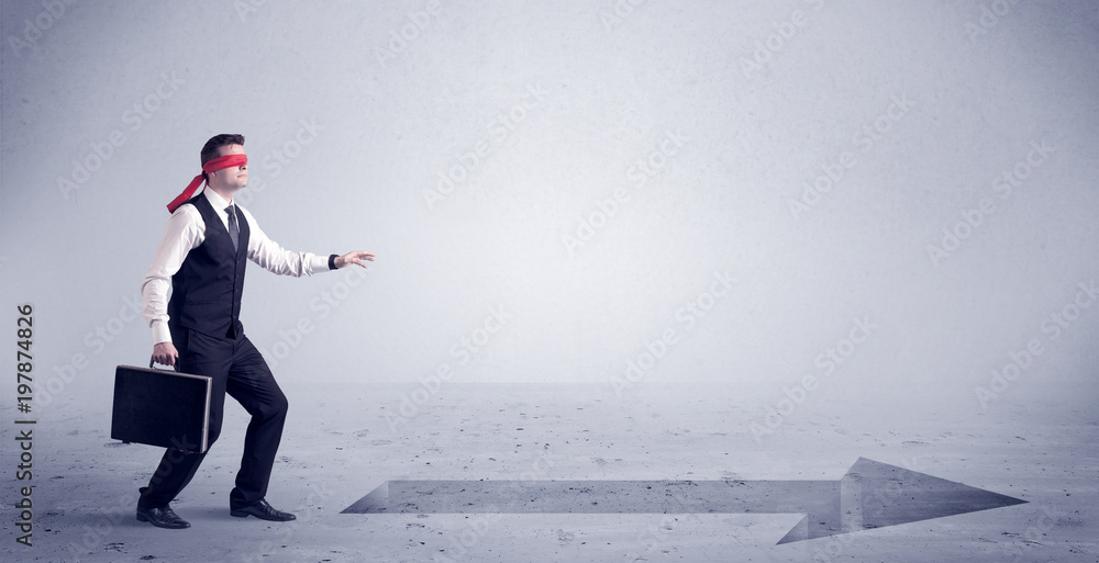 A confused blind salesman standing in front of a drawn arrow on the floor pointing in the right direction concept. A confused blind salesman standing in front of a drawn arrow on the floor pointing in the right direction concept.