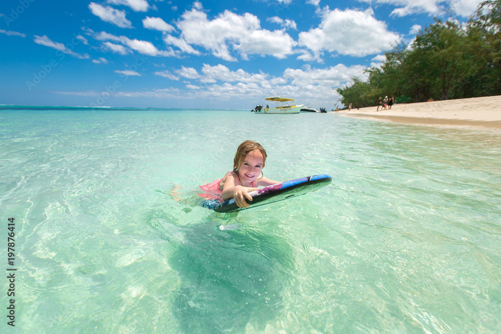 Little baby girl - young surfer with bodyboard has a fun on small ocean waves. Active family lifestyle