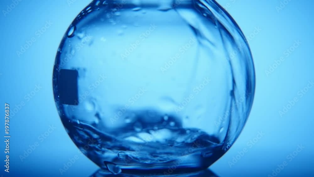 An impressive macro shot of a large round glass flask filled with a narrow stream of crystaline water in the blue background An impressive macro shot of a large round glass flask filled with a narrow stream of crystaline water in the blue background
