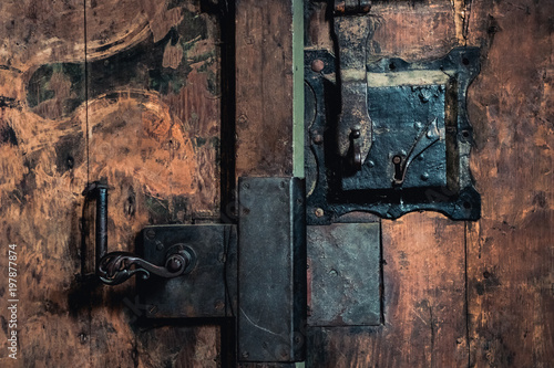 Close-up photo of an old rusty metal lock mechanism on a wooden door.