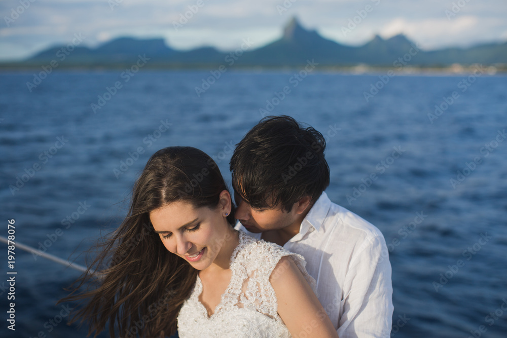 .Beautiful wedding couple bride and groom on yacht at wedding day outdoors in the sea. Happy marriage couple kissing on boat in ocean. Stylish Marine wedding.
