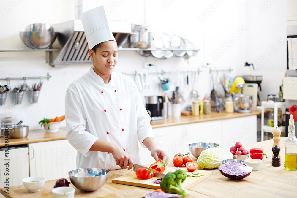 Young chef in uniform cutting fresh red pepper for salad or vegetable stew in the kitchen Young chef in uniform cutting fresh red pepper for salad or vegetable stew in the kitchen