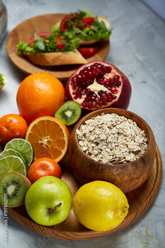 Bowl with oatmeal flakes served with fruits on wooden tray over rustic background, flat lay, selective focus