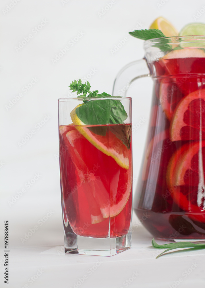 A glass with red sangria and oranges, lime and lemon on a white background. Behind the jug.Close up. Copy-space. A glass with red sangria and oranges, lime and lemon on a white background. Behind the jug.Close up. Copy-space.