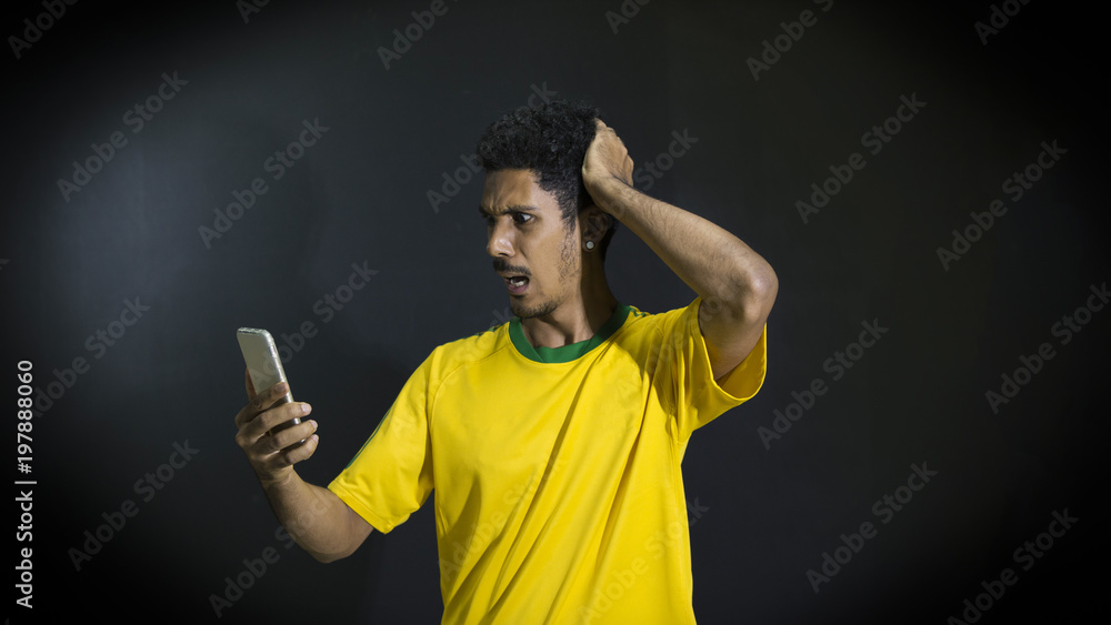 Male athlete or fan in yellow uniform looking cell phone on black background