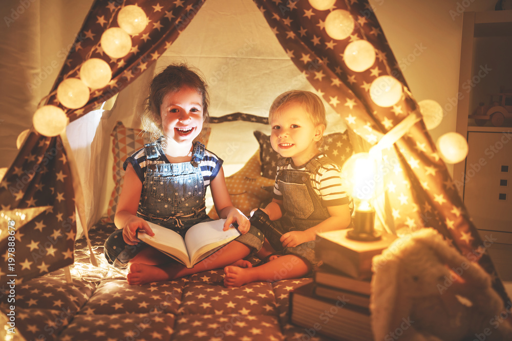 children boy and girl reading book with  flashlight in  tent