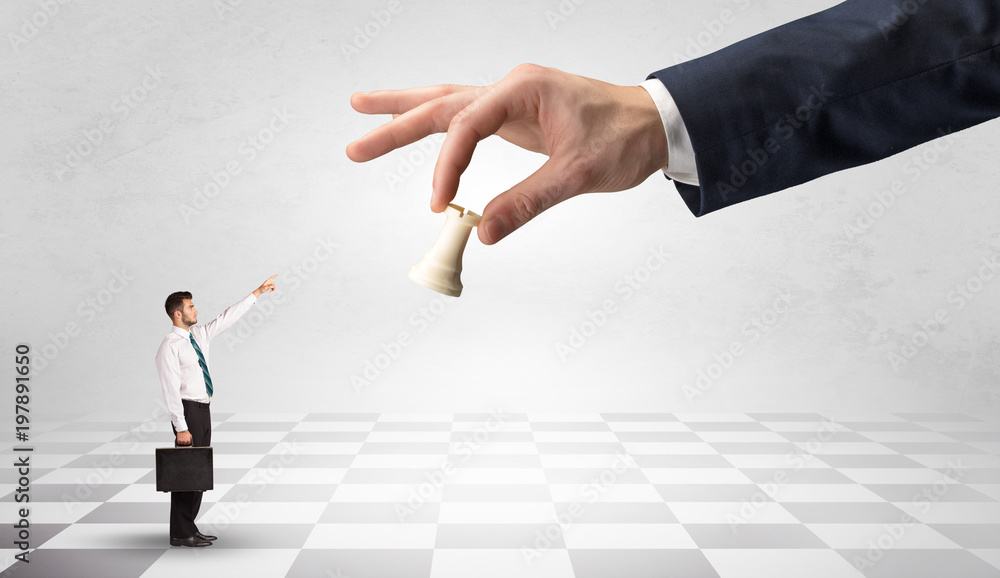 Fototapeta premium Small businessman fighting against big chessman on a big hand with chess board concept
