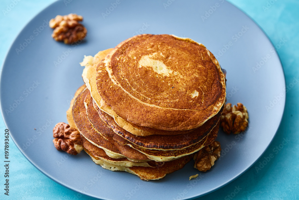 Pile of homemade pancakes with walnuts on blueish plate over blue background, selective focus Pile of homemade pancakes with walnuts on blueish plate over blue background, selective focus