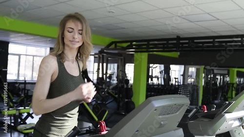Athletic girl running on a treadmill in front of the window in gym.