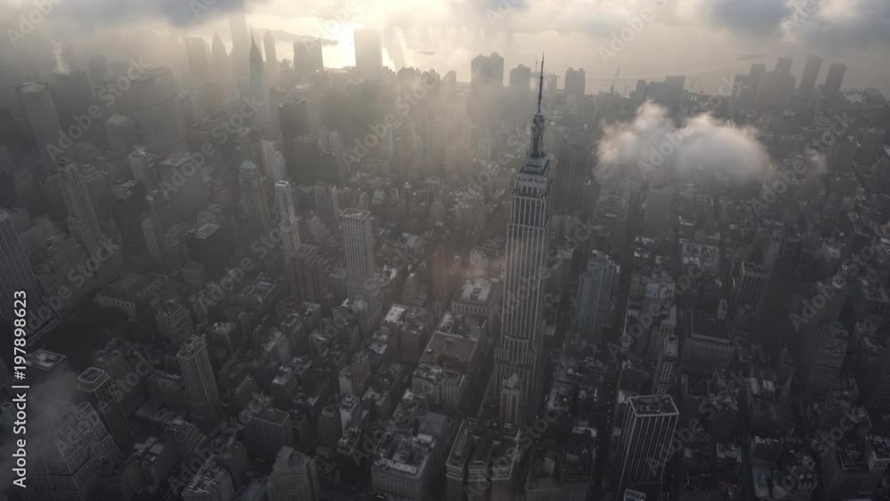 New York City high angle aerial view of Midtown Manhattan skyscrapers, approaching the Empire State Building with low level clouds at sunrise.