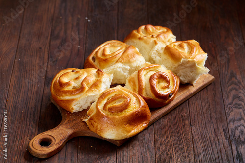 Homemade rose buns on wooden cutting board over rustic vintage background, close-up, shallow depth of field photo