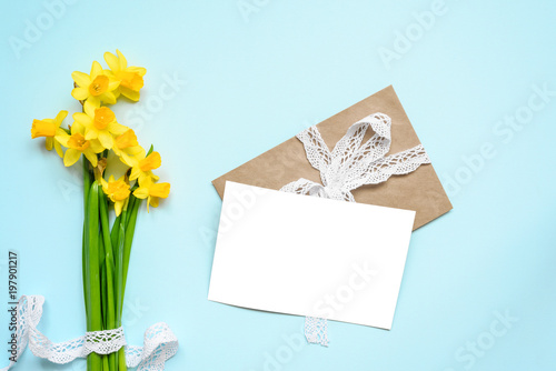 Fototapeta Naklejka Na Ścianę i Meble -  blank white greeting card with spring yellow narcissus flowers bouquet over blue background. mock up
