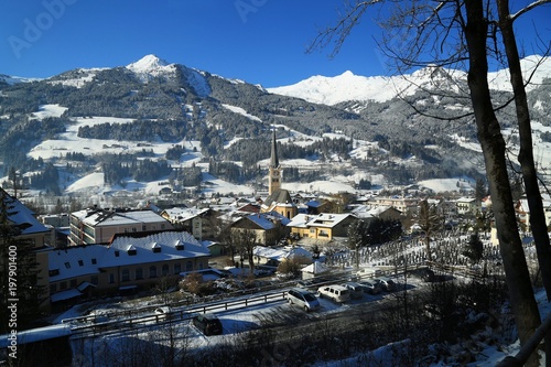 Winter view of town Bad Hofgastein, Austria from top of a hill on bright sunny day with clear blue sky. Famous destination, ski resort. Church, houses, trees, cemetery.