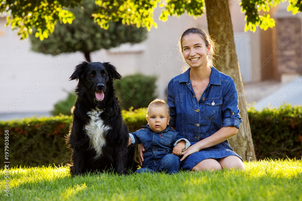 A mother with baby son and black dog in green neighborhood