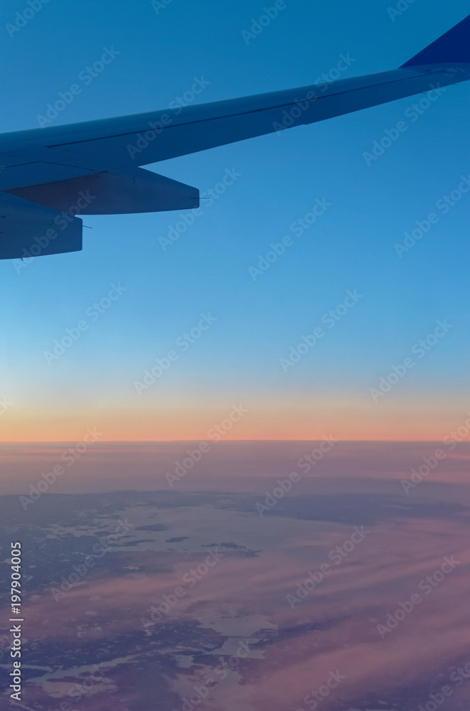 Airplane wing over landscape and cloudy sky at sunset Airplane wing over landscape and cloudy sky at sunset