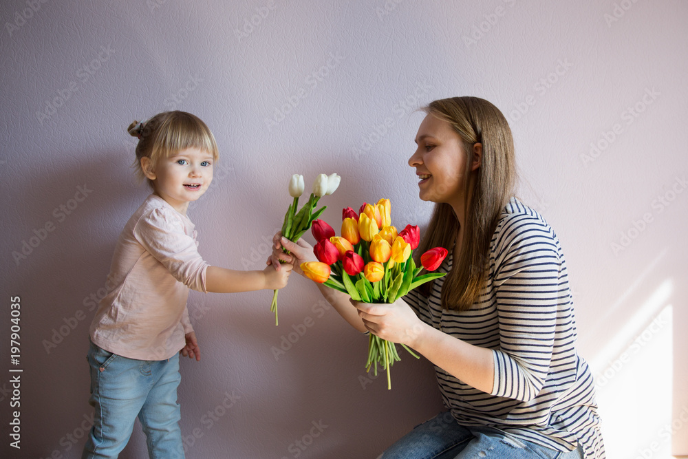 Happy family. Daughter gives a bouquet of flowers (tulips) to her mother in the room. Naturally laughed. Mother's Day. Happy family. Daughter gives a bouquet of flowers (tulips) to her mother in the room. Naturally laughed. Mother's Day.