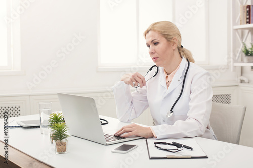Serious female doctor typing on laptop