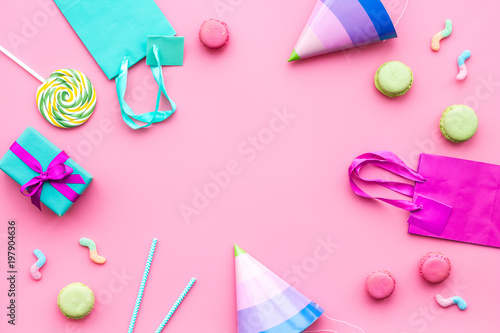 Birthday party accessories. Party hat, sweets, paper bag for gift on pink background top view copy space mockup