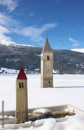 Sunken clock tower in Resia iced lake and its wooden miniature. Val Venosta, Sud Tirol, Italy