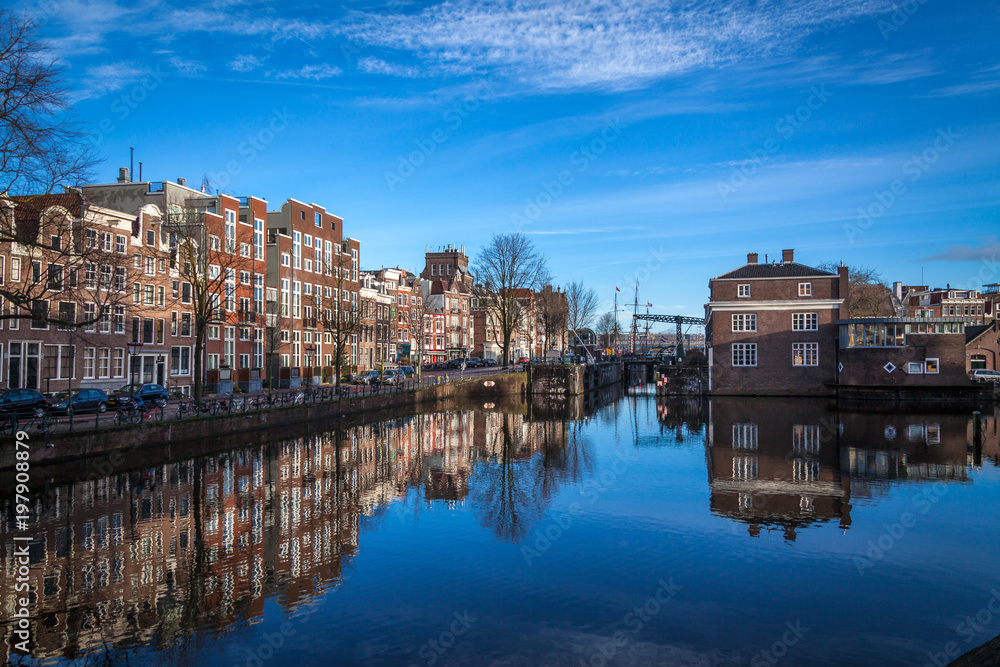 water canals in Amsterdam with blue waters and blue sky on a sunny day with a reflection of traditional buildings in canal's waters