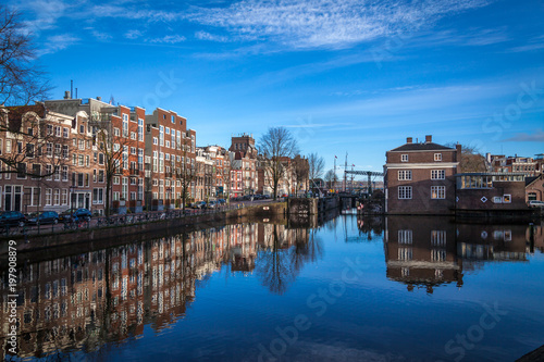 water canals in Amsterdam with blue waters and blue sky on a sunny day with a reflection of traditional buildings in canal s waters