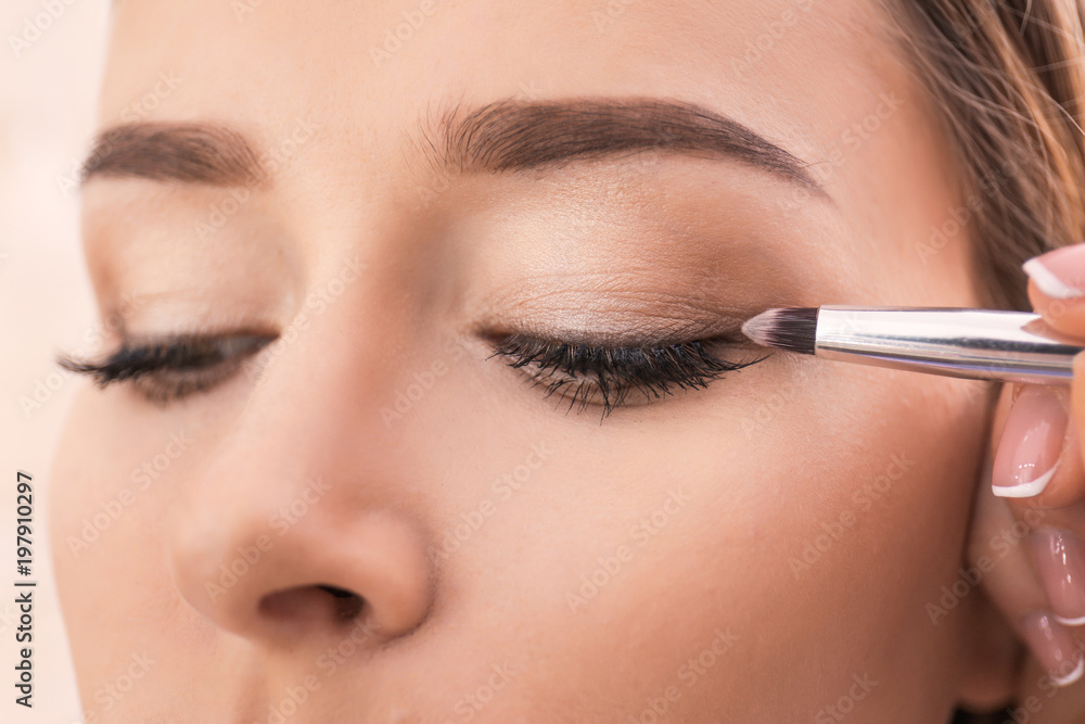 Professional visage artist applying makeup on woman's face in salon, closeup